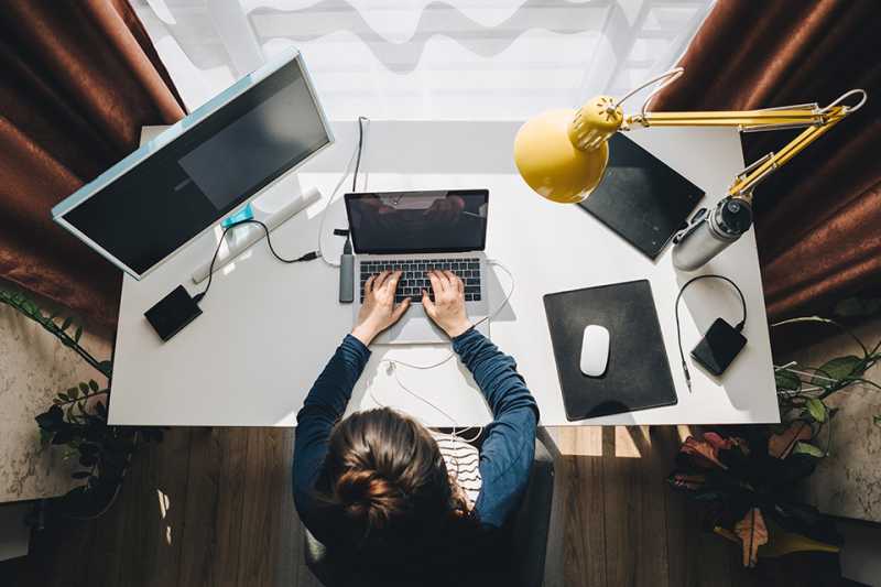 Frau sitzt im Homeoffice beim Schreibtisch und arbeitet am Laptop